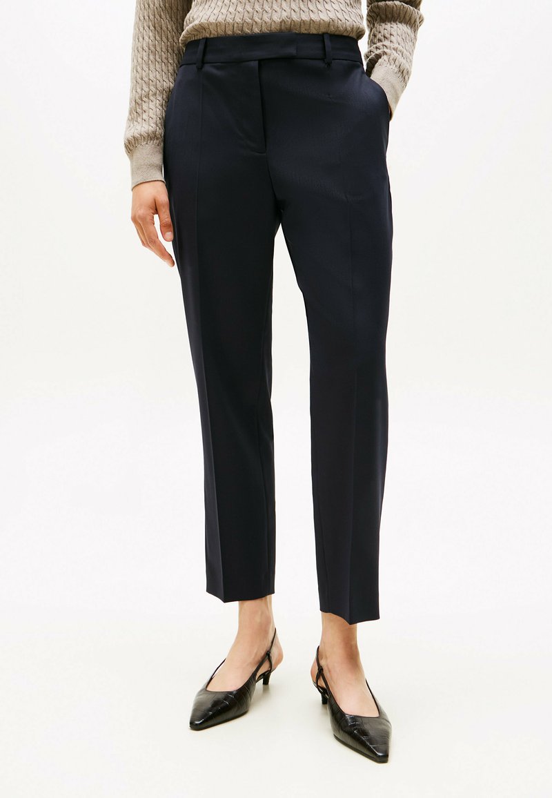 Marineblauwe, op maat gemaakte broeken met een gladde textuur, voorzien van voorplooien en een slim fit, gecombineerd met zwarte, puntige slingback hakken.