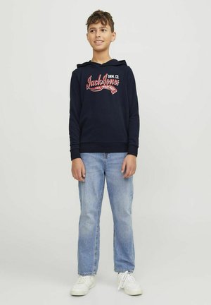 Sudadera azul marino con logo frontal, capucha con cordón, puños de canalé, combinada con jeans rectos de un azul claro y zapatillas blancas.