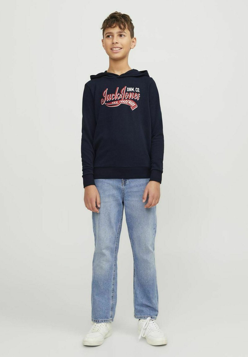 Sudadera azul marino con logo frontal, capucha con cordón, puños de canalé, combinada con jeans rectos de un azul claro y zapatillas blancas.