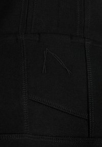 Tessuto nero con una texture liscia, caratterizzato da cuciture visibili e un piccolo accento triangolare nell'intreccio.