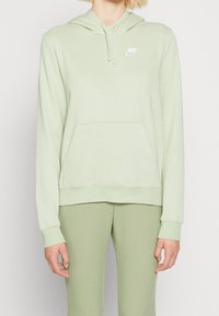 Ljusgrön Nike-hoodie med kängurufickor, dragsko på huvan och vit logotyp på bröstet. Mjuk, slät tyg med ribbade muddar.