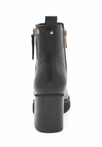 Botín de cuero negro hasta el tobillo con tacón cuadrado, cremallera dorada en el lateral y tira en la parte trasera, mostrado desde la vista trasera sobre un fondo blanco.