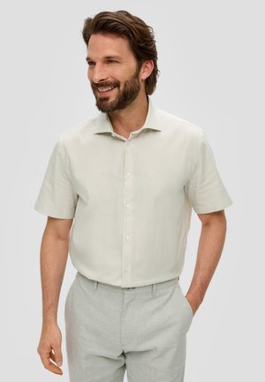 Lichtbeige korte mouwen knoopshirt met een zachte textuur, voorzien van een puntige kraag en witte knopen, gedragen met lichtgrijze broeken.
