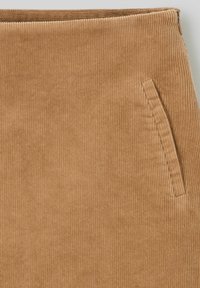 Jupe en velours côtelé marron avec une texture à nervures verticales, détail de poche latérale et ceinture lisse. Fermeture éclair à l'arrière.