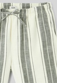 Pantalons en mélange de lin avec taille élastique et cordon de serrage. Présente des rayures en chevron noir et blanc sur un fond clair.