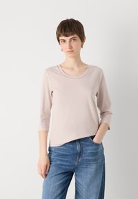 Lichtroze languit-shirt met een ronde halslijn en een zachte textuur, gecombineerd met hooggerijpte blauwe jeans. Eenvoudig en gestroomlijnd ontwerp.