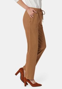 Bruine broek met elastische taille en zijzakken, taps toelopend design en een gladde textuur, in combinatie met bruine hoge hakken.