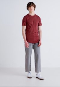 T-shirt a maniche corte color marsala, jeans dritti grigi, sneaker bianche con dettagli marroni. Design semplice, texture liscia, silhouette aderente.