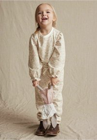 Bloemenprint jumpsuit met lange mouwen en gerimpelde manchetten, met een strik taille en een roze en witte accessoire. Bruine schoenen maken de outfit compleet.