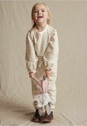 Bloemenprint jumpsuit met lange mouwen en gerimpelde manchetten, met een strik taille en een roze en witte accessoire. Bruine schoenen maken de outfit compleet.
