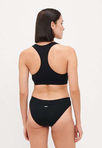 Black ribbed sports bra with a racerback design, paired with matching bikini briefs. Features a small metallic logo on the waistband.