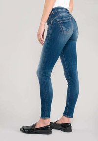Jeans skinny in denim blu scuro, design a vita alta, con tasche posteriori e cuciture sottili. Abbinati a scarpe nere basse.
