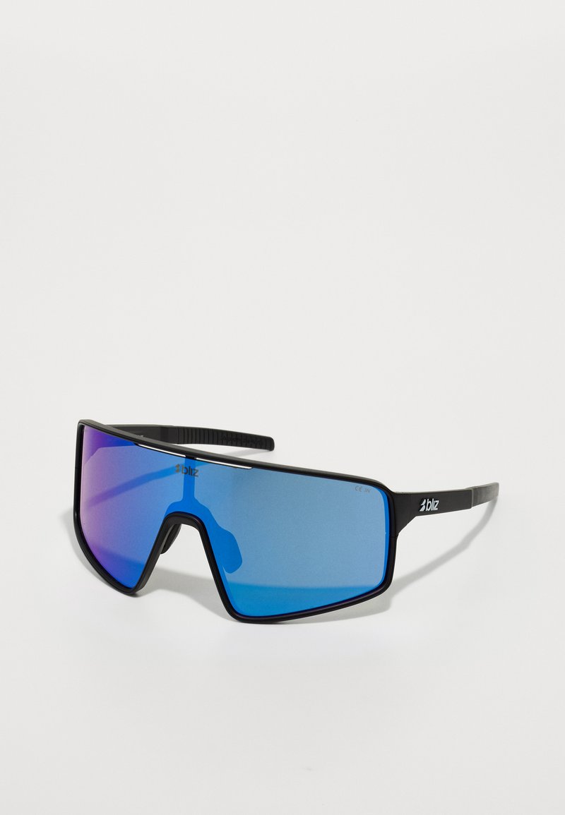 Lunettes de soleil avec une grande monture noire angulaire et des verres dégradés bleus. Les branches texturées affichent le logo de la marque. Surface des verres lisse et réfléchissante.