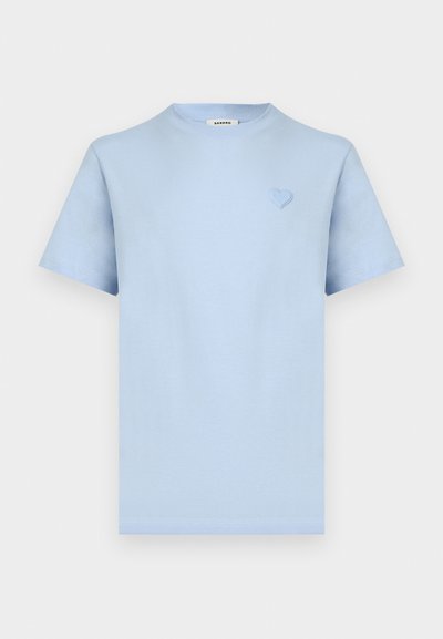 Svetlo modra kratka majica s klasičnim okroglim ovratnikom, z majhnim vstavljenim srcem na levi strani prsi in etiketo Sandro na ovratniku.