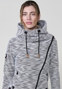 Szürke, texturált kapucnis pulóver, cowl nyakkal, fekete díszítésekkel, húzózsinórokkal és finom mintázattal. Oldalán cipzár és logó címke található az ujjon.