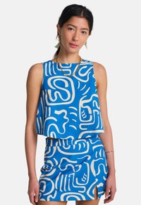 Σετ με μπλε crop top και φούστα με αφηρημένα λευκά σχέδια. Το ύφασμα φαίνεται υφασμένο με άνετη, χαλαρή εφαρμογή και λεπτομέρεια με άνοιγμα στο πλάι.