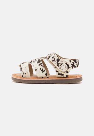 Sandalias de cuero de vaca en blanco con manchas negras, con tres correas anchas y una suela acolchada en color marrón. Diseño abierto en la parte trasera para facilitar su uso.