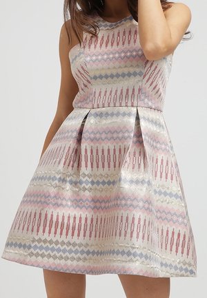 Vestido de línea A sin mangas con patrones geométricos y verticales en tonos pastel en rosa, azul y beige sobre una tela brillante, llevado por una persona de pie.