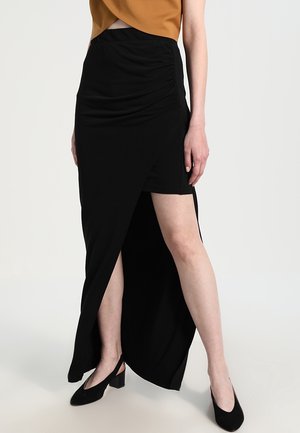 Woman wearing a black asymmetrical skirt with a high slit on left leg, paired with black slingback heels and a brown cropped top.