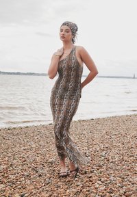 Leopard uzorak, uska haljina bez rukava s malo proširenim rubom. Nošena uz ravne sandale i odgovarajuću traku za glavu, na šljunčanoj plaži.