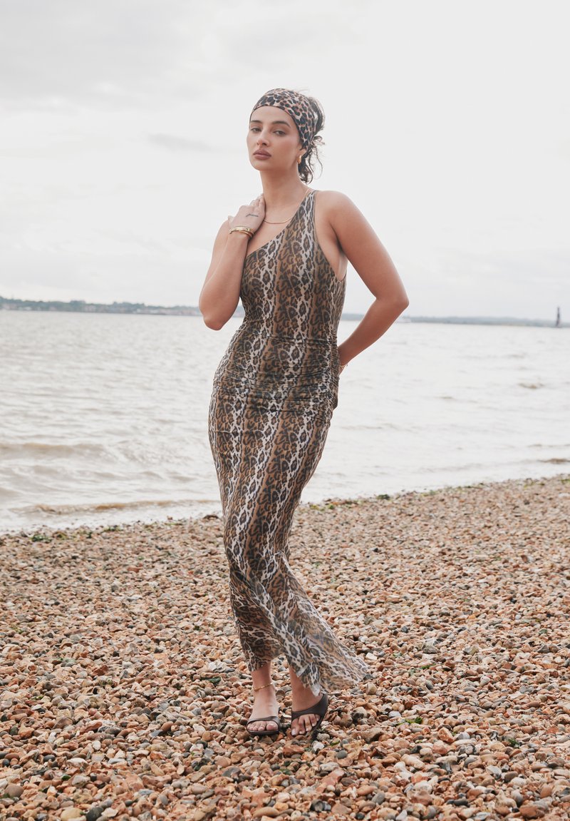 Leopard uzorak, uska haljina bez rukava s malo proširenim rubom. Nošena uz ravne sandale i odgovarajuću traku za glavu, na šljunčanoj plaži.