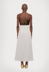 Brun satin camisole med tynne stropper, paret med et hvitt maxiskjørt. Har en glatt tekstur og et flowy design, komplementert av brune platåhæler.