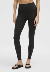 Zwarte high-waisted leggings met een gladde textuur, voorzien van subtiele stippenpatronen, een aansluitend ontwerp en een enkellange snit, gecombineerd met zwarte slipper.