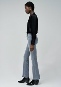 Camisa de satén negra, jeans de campana gris claro y botas de tobillo negras con tacón. Diseño simple con texturas suaves y detalles mínimos.