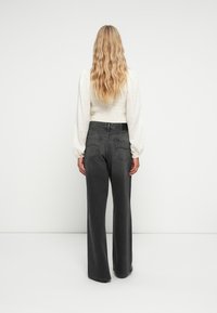 Jeans a vita alta e gamba larga in denim nero lavato. I dettagli includono una zip nella parte anteriore, tasche posteriori e una texture liscia con cuciture doppie.