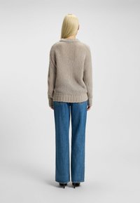 Beige gebreid trui met een losse pasvorm, voorzien van een ribbeltextuur en een iets verlaagde schouder, gecombineerd met wijde denim jeans.