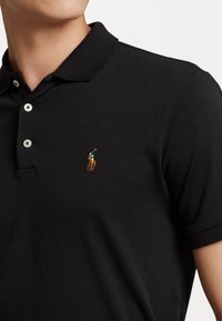 Homme portant un polo noir avec un petit logo brodé d'un joueur de polo à cheval sur le côté gauche de la poitrine.