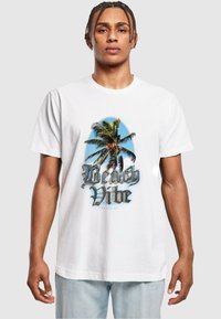 Balta medvilninė marškinėliai su grafiniu dizainu, vaizduojančiu palmę ir tekstu "Beach Vibe" drąsiais, 3D šriftais. Atsitiktinė forma, trumpomis rankovėmis.
