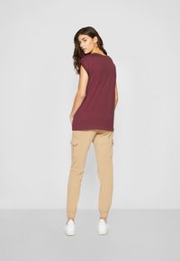 Bordeaux oversized T-shirt med korte ærmer, parret med beige cargo bukser med elastiske manchetter og sidelommer, suppleret med hvide sneakers.