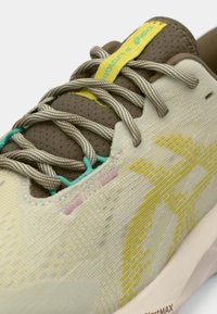 Baskets présentant un dessus texturé jaune clair avec un motif jaune, des accents marron et des lacets teal. La semelle est rembourrée et de couleur blanc cassé.