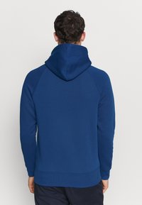Sudadera azul marino con capucha ajustable, mangas raglán y puños y dobladillo de canalé. Textura suave, diseño sencillo y sin patrones visibles.