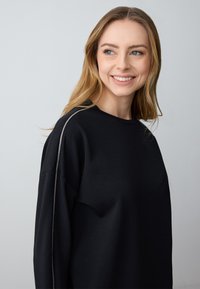 Black crew-neck sweatshirt made of soft fabric, featuring a textured silver accent along the shoulder seams. Relaxed shape with dropped shoulders.