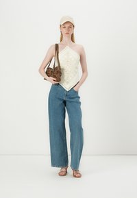 Háčkovaný krémový halter top, svetlomodré široké nohavice, hnedá taška a béžová čiapka; prezentované textúrované vzory a neutrálne odtiene.