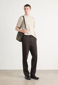 Beige rövid ujjú ing, sötét nadrág, fekete cipők és zöld crossbody táska cipzárokkal. Simára pfelület, egyszerű dizájn és semleges színek.