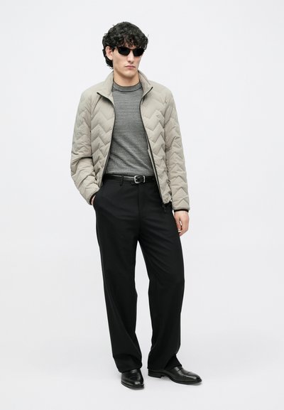 Világosszürke steppelt dzseki magas gallérral, szürke mintás hosszú ujjú ing, fekete nadrág és fekete cipő. A modell napszemüveget visel.