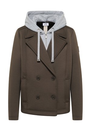 Donkergroene double-breasted jas met grote revers, gedragen over een lichtgrijze zip-up hoodie met trekkoorden.