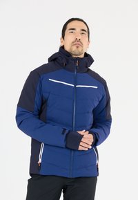 Marinblå isolerad jacka med huva, med kontrasterande mörkblå ärmar, vita ränder, frontdragkedja och elastiska manschetter.