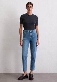 Czarna, prążkowana bluzka z krótkim rękawem, noszona z jasnoniebieskimi dżinsami z wysokim stanem i ciemnymi mokasynami. Gładkie tekstury, dopasowana bluzka i proste nogawki dżinsów.