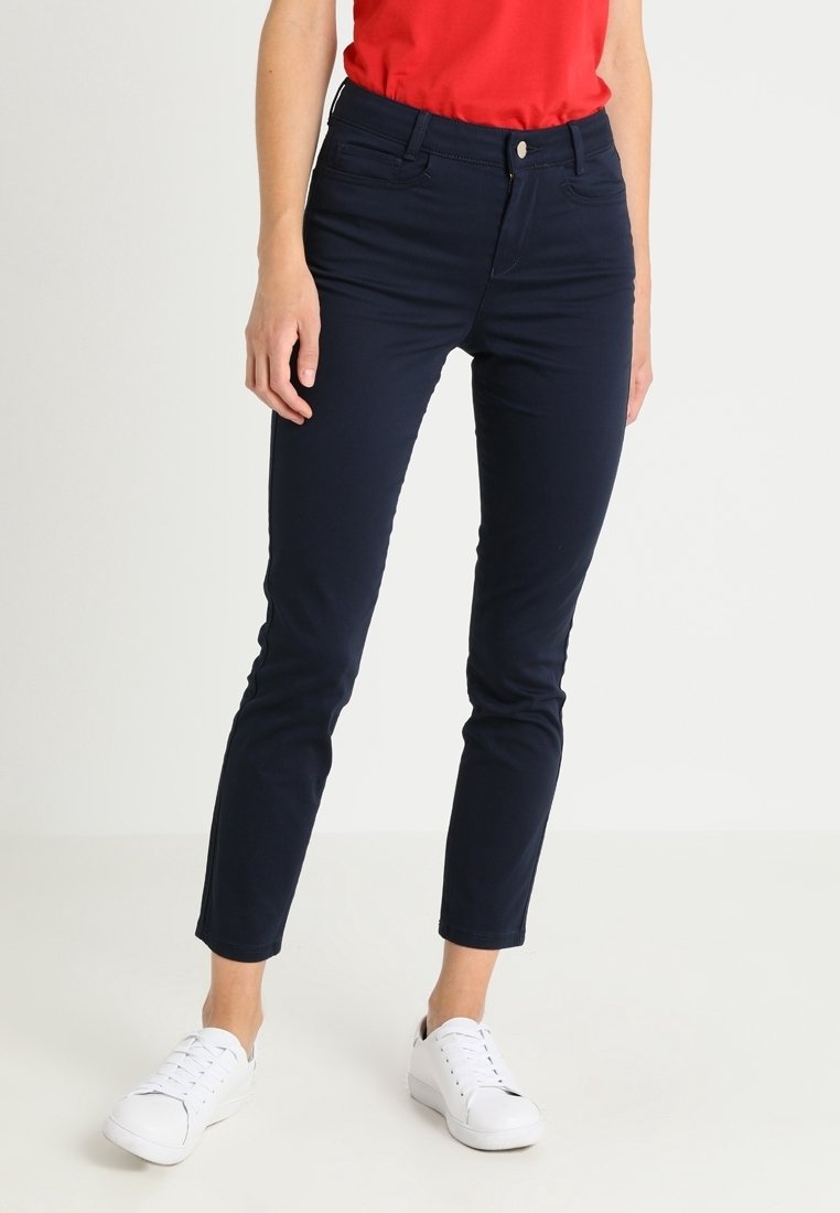 Navyblauwe slim-fit broek van een katoenmix met zijzakken en een knoopsluiting, gecombineerd met witte sneakers en een rode top.
