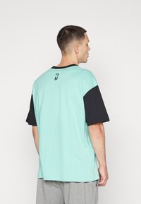 Camiseta verde menta con mangas cortas negras y un detalle en el cuello negro. Presenta un pequeño logo impreso en la parte superior de la espalda. Fabricada en algodón.