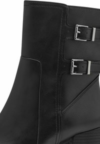 Bottine noire en cuir avec une texture lisse, tige inclinée et deux boucles en métal argenté sur le côté extérieur pour un ajustement réglable.