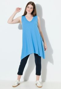 Top azul sin mangas con escote en V y dobladillo asimétrico, combinado con pantalones marinos con detalles de encaje. Zapatillas blancas completan el conjunto.