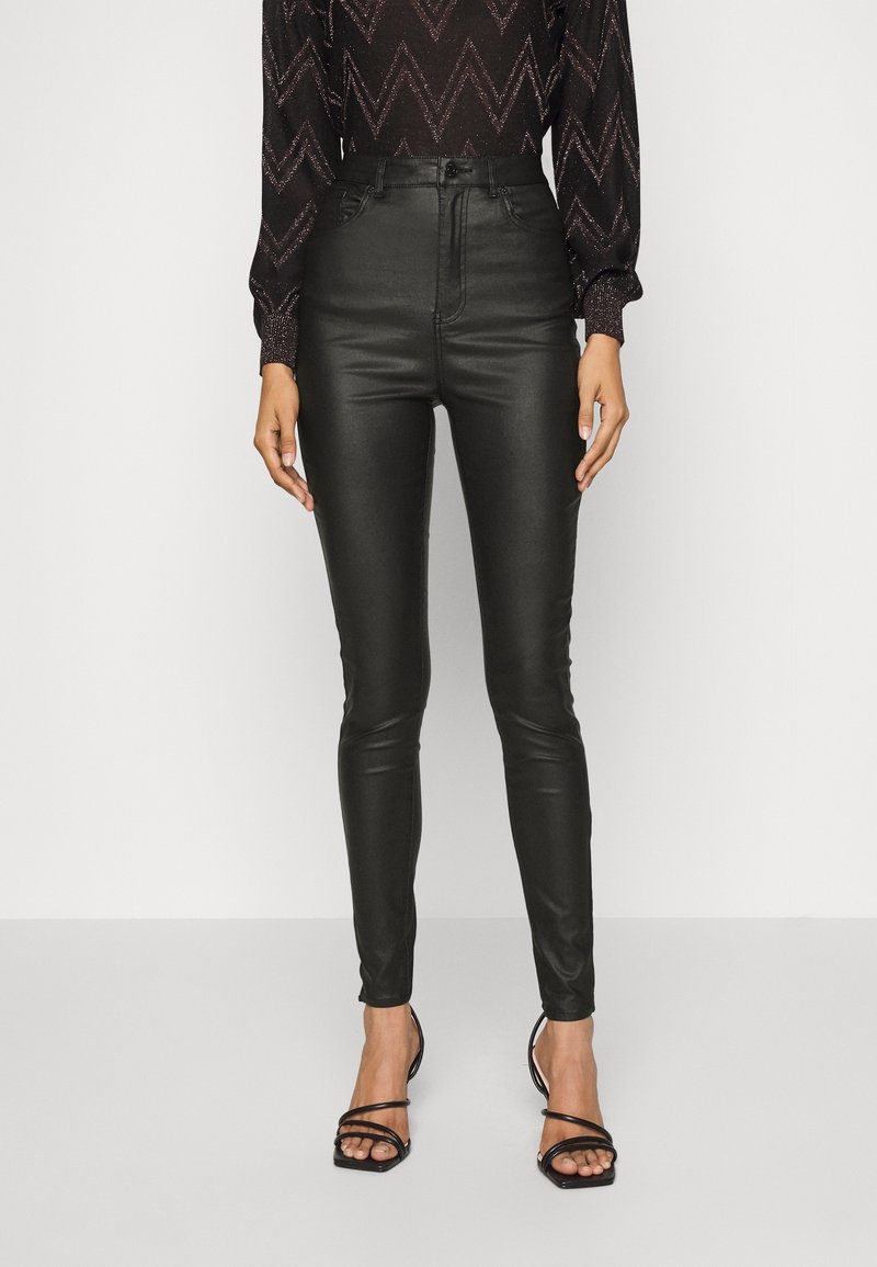 Svarta höga fusk läderbyxor med smal passform, med en slät textur och minimal detaljering, i kombination med svarta sandaler med remmar.