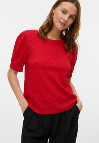 Top corto a maniche corte rosso con texture, collo rotondo e maniche a palloncino, abbinato a pantaloni neri larghi.