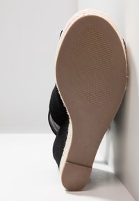 Sandale plateforme en daim noir avec une semelle texturée de style espadrille, équipée d'une semelle inférieure en caoutchouc brun lisse et d'un talon court et arrondi.