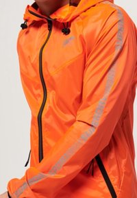 Veste à capuche orange vif avec fermeture éclair noire et cordons de serrage, arborant le texte réfléchissant "Superdry Sport" le long de la manche droite.